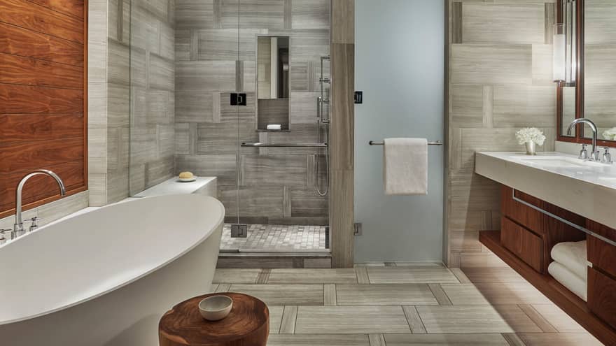 Ocean View Suite bathroom with white soaker tub under wood accent wall, glass walk-in shower, sink