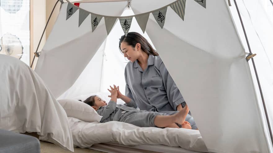Parent and child in pyjamas playing together inside a cozy tent with bunting decorations