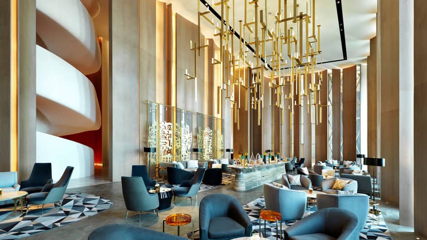 Modern dining chairs, tables in lounge with soaring ceilings, gold sculptures hanging from ceiling, wall