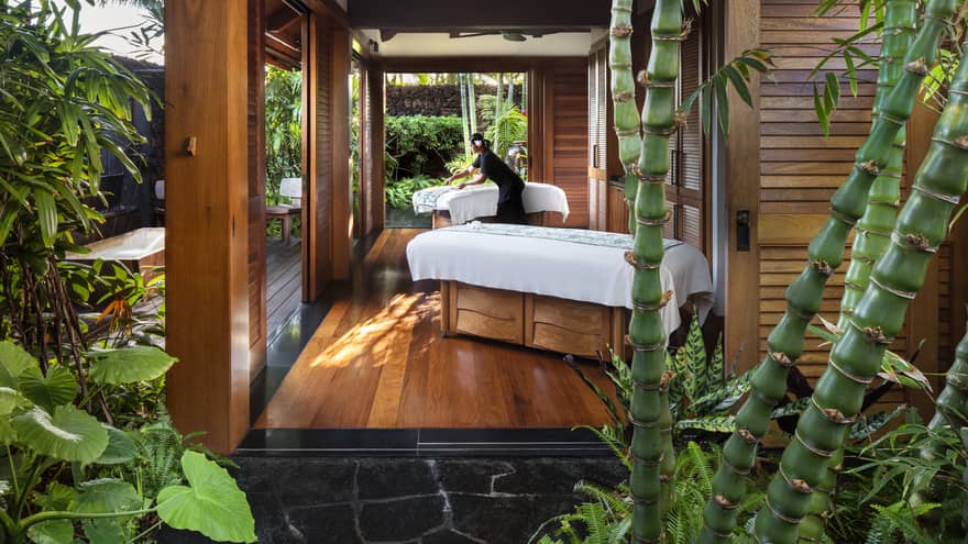 Spa staff spreads sheet on couples massage beds on open-air pavilion 