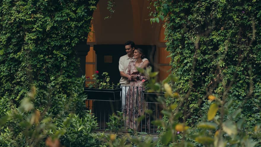 Couple standing on a balcony covered by lush greenery, enjoying a peaceful moment surrounded by nature in an intimate, serene garden setting.