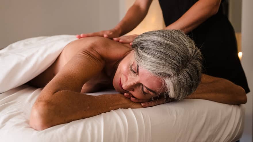 Person lies face down on massage table as therapist in black uniform performs massage
