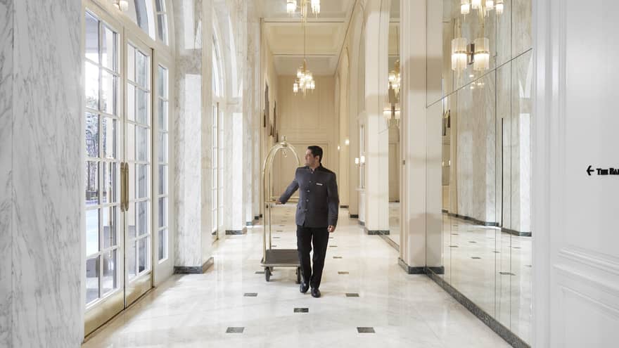 A team member walking with a luggage cart through a bright white and well lit hallway.