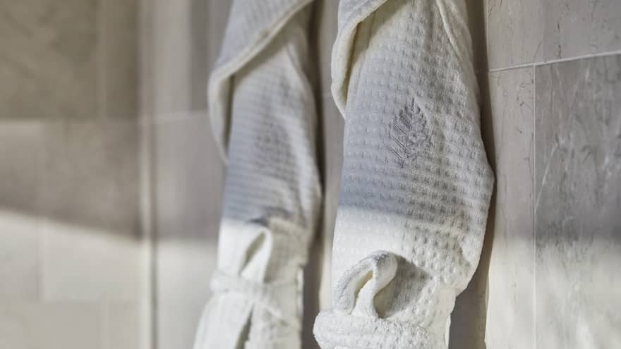 Two spa robes hanging on a wall of smooth tile.