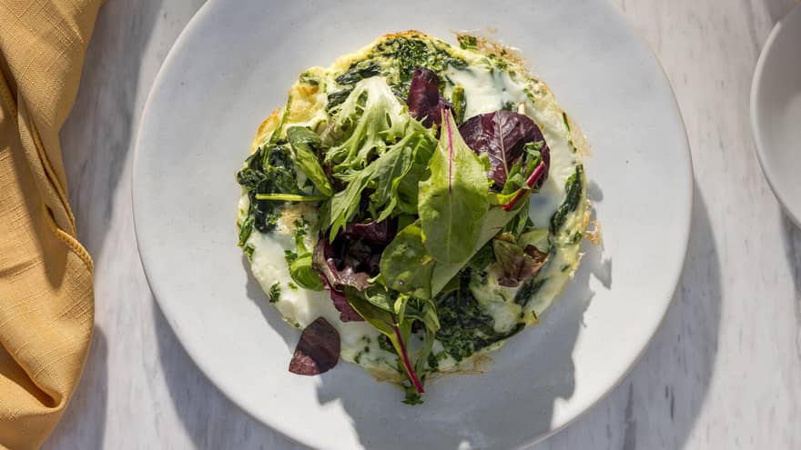 A colourful egg dish topped with greens, served on a white dish