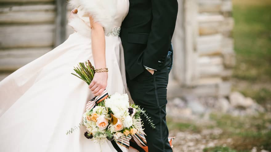 Close-up of a couple dressed in wedding attire, with one partner in a black suit and the other holding a bouquet of flowers
