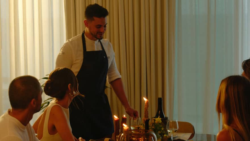 Group of four sits for a meal in a private residence while a chef brings the plates