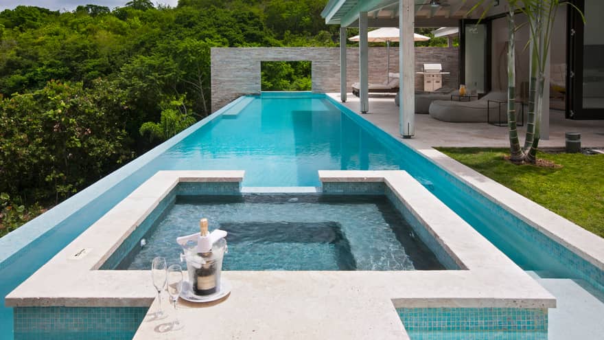 Champagne, two glasses on edge of residence whirlpool, long outdoor swimming pool