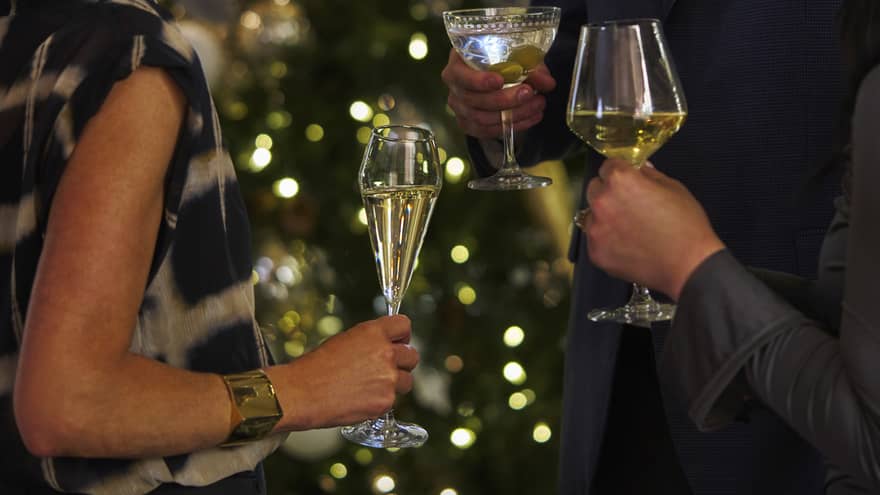 Three people wearing festive attire stand together talking, each holding a stemmed cocktail glass in one hand