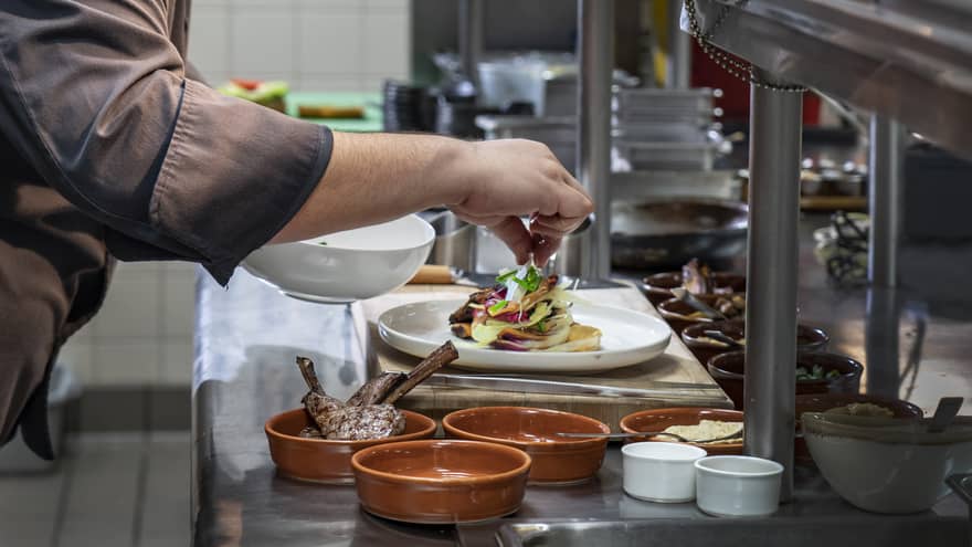 Chef garnishes gourmet meat entree on steel kitchen line