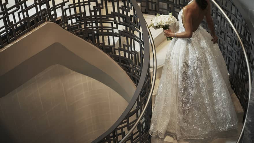 Bride wearing long white wedding gown walks up spiral staircase