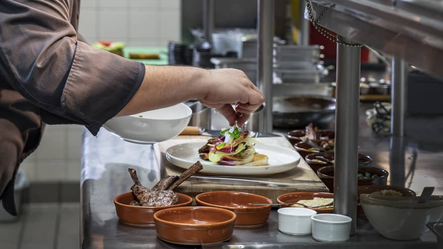 Chef garnishes gourmet meat entree on steel kitchen line