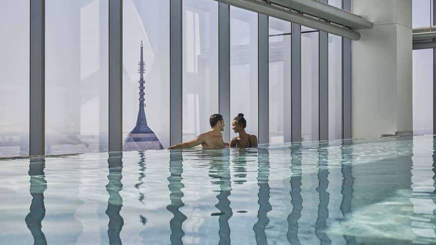 A man and woman stand close to one another in the pool overlooking downtown Philadelphia