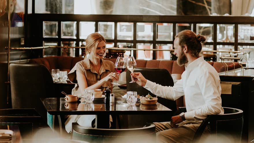 Smiling couple at table toasts with wine glasses in restaurant lounge 