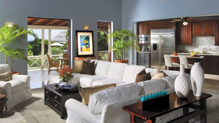 Plush white sofas by wood table, modern white vases, kitchen in background