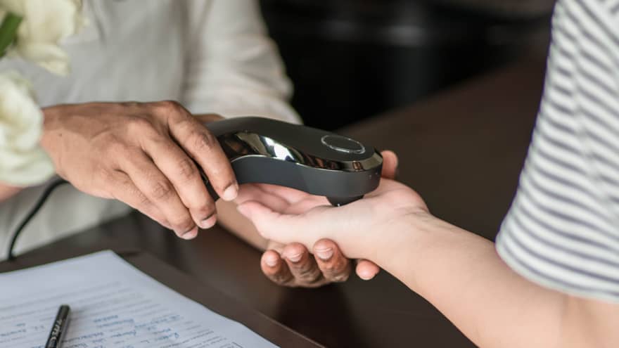 Close-up of a person receiving a spa treatment, with a therapist using a handheld device on their hand, alongside a clipboard with paperwork on the table.