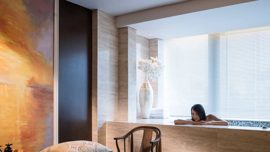 Woman rests head, arms on Spa tub beside massage table