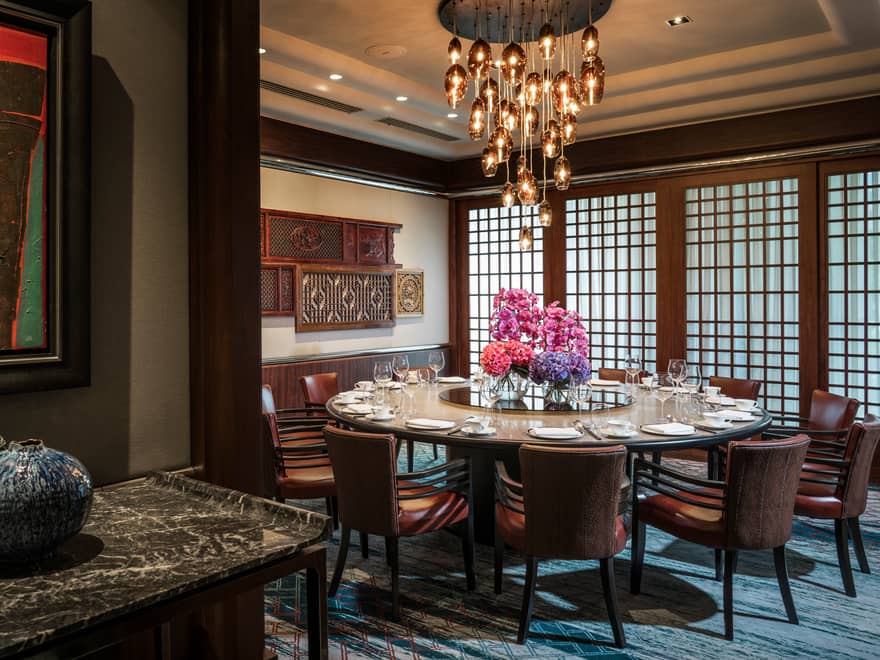 Round private dining table with pink flowers under modern hanging lights, wood carvings on wall