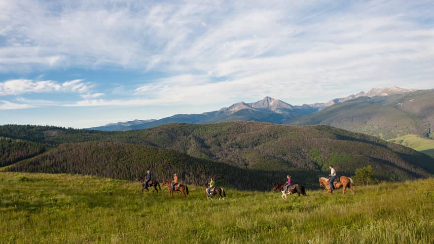 A group of people on horseback riding along grass and hills.