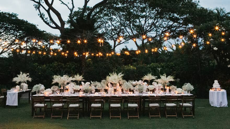 Garden wedding reception set up, long dining table with white flowers under string lights
