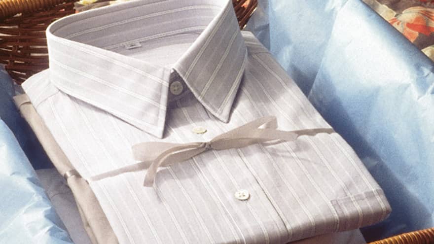 Folded men's dress shirt tied in package with bow under open tissue paper in wicker basket 