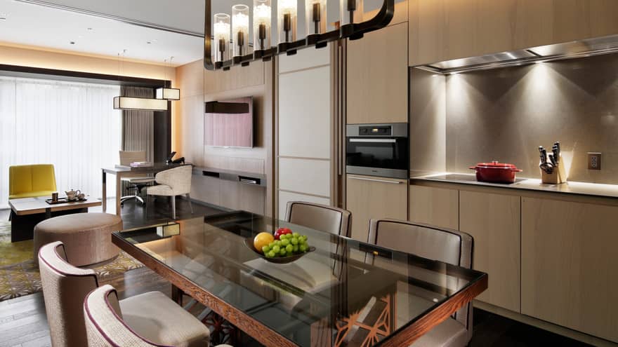 Modern open-plan living and dining area with a glass dining table, kitchenette and cozy seating area