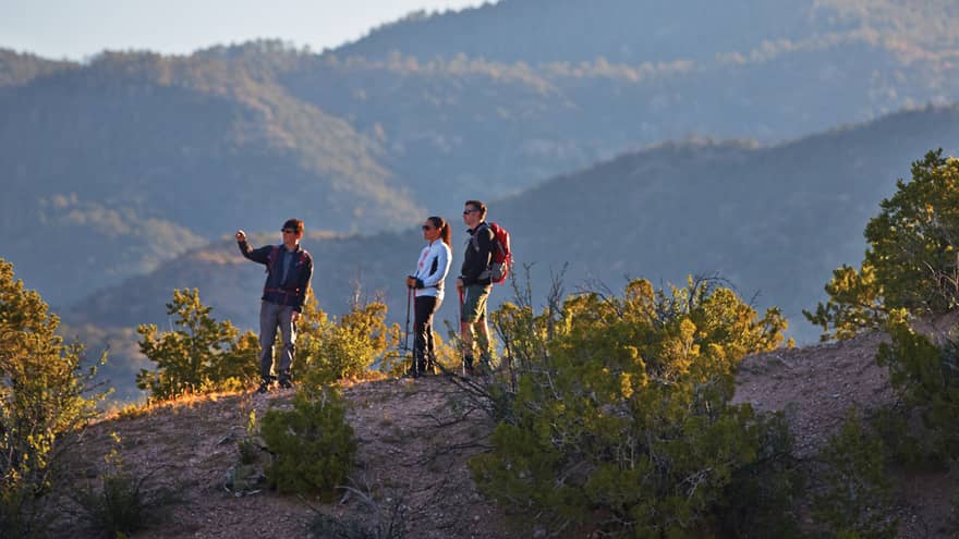 Three people hike on desert mountain hill