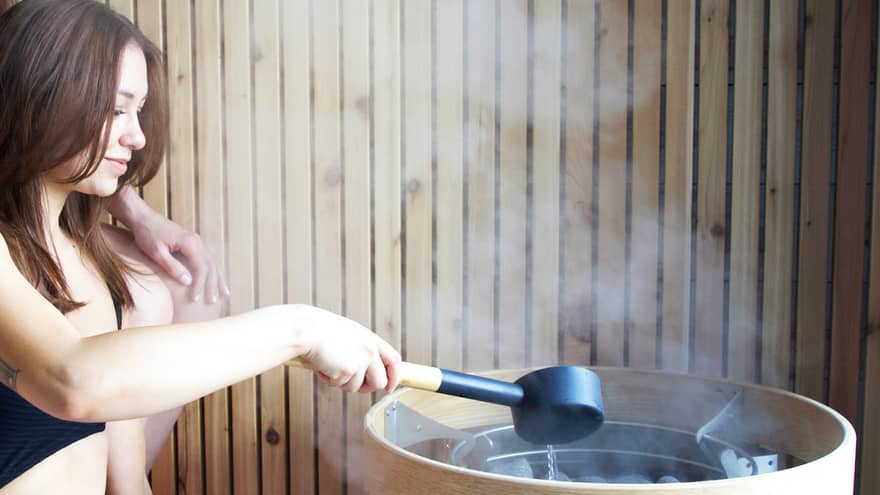 Two women pouring water onto hot rocks creating steam.