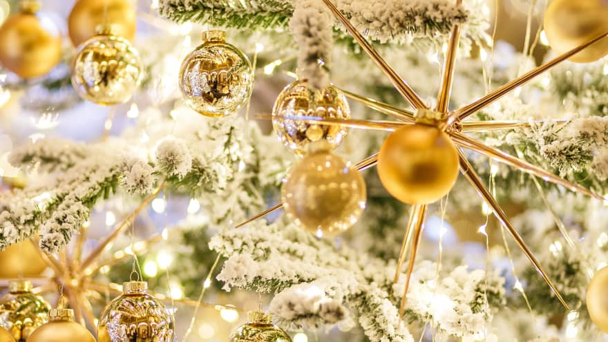 Several golden ornaments on a snow covered Christmas tree. 