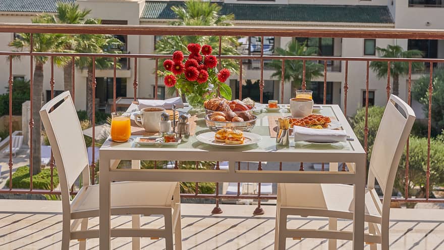 Outdoor table with flowers and elaborate breakfast spread on a balcony overlooking Tunis and water