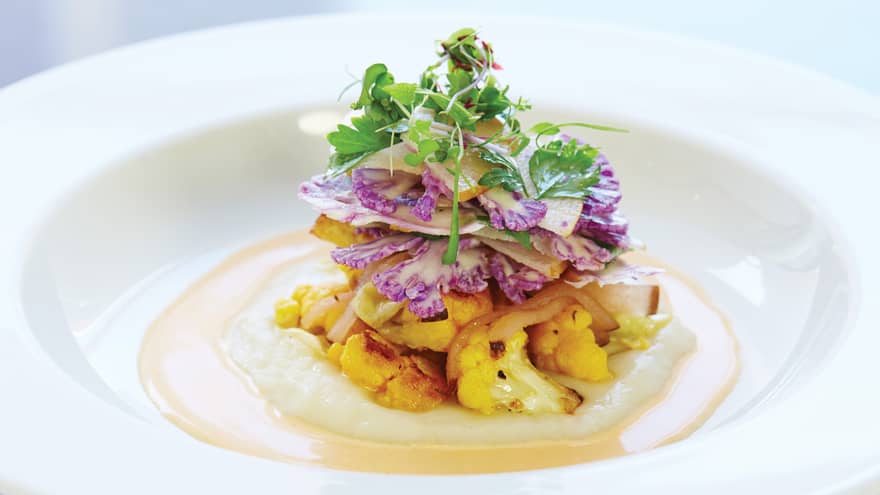 Close-up of white dish with roasted cauliflower and puree, garnished with fresh herbs