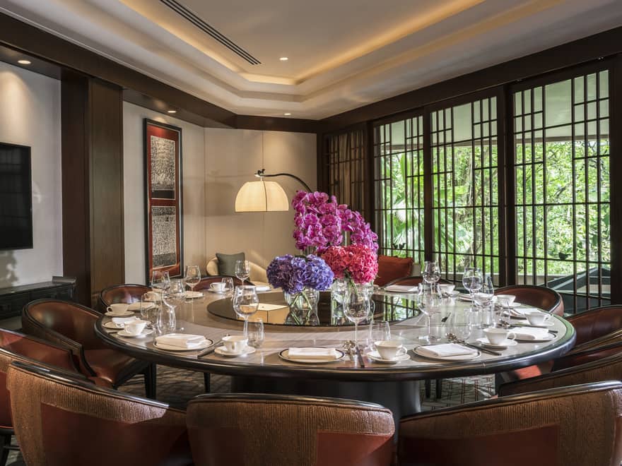 Round private dining meeting table with large pink floral display in centre, TV on wall