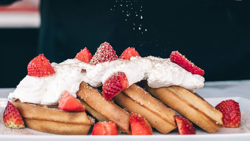 Close-up of waffles topped with whipped cream and strawberries, chef shaving cinnamon stick