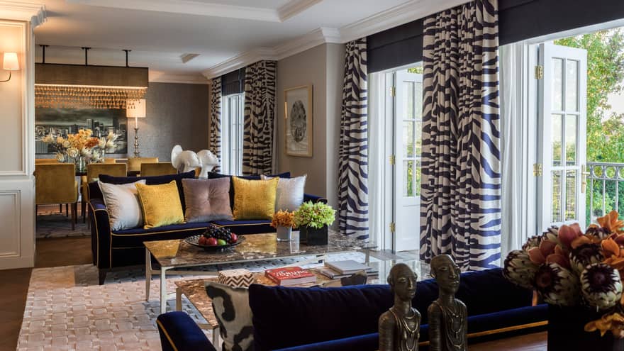 Royal Suite sitting area, two blue sofas with yellow, grey pillows, open patio doors with Zebra print curtains