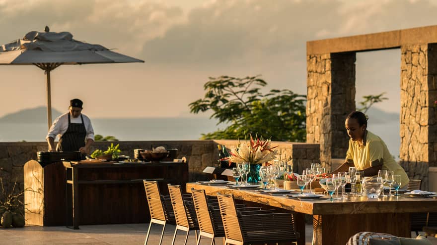Six-Bedroom Residence Villa close-up of server setting long dining table by swimming pool at sunset 