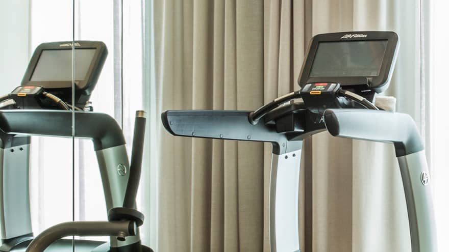 Cardio exercise machines, rack of hand weights near windows with long curtains in fitness centre