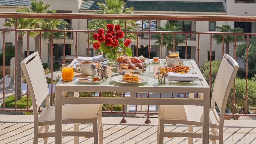Outdoor table with flowers and elaborate breakfast spread on a balcony overlooking Tunis and water