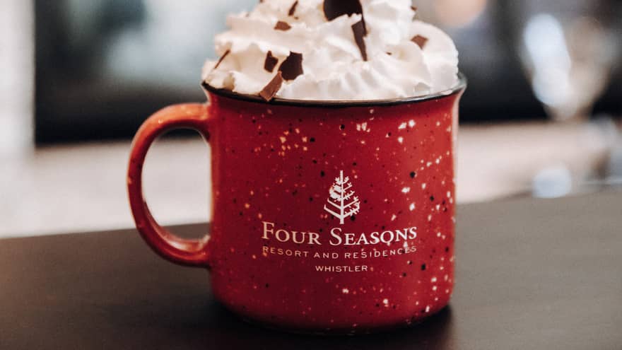 Red enamel mug with Four Seasons logo filled with hot chocolate and overflowing with whipped cream