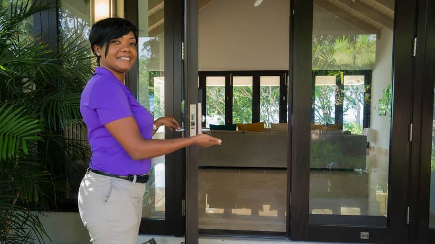 Smiling villa ambassador holds open glass door to estate
