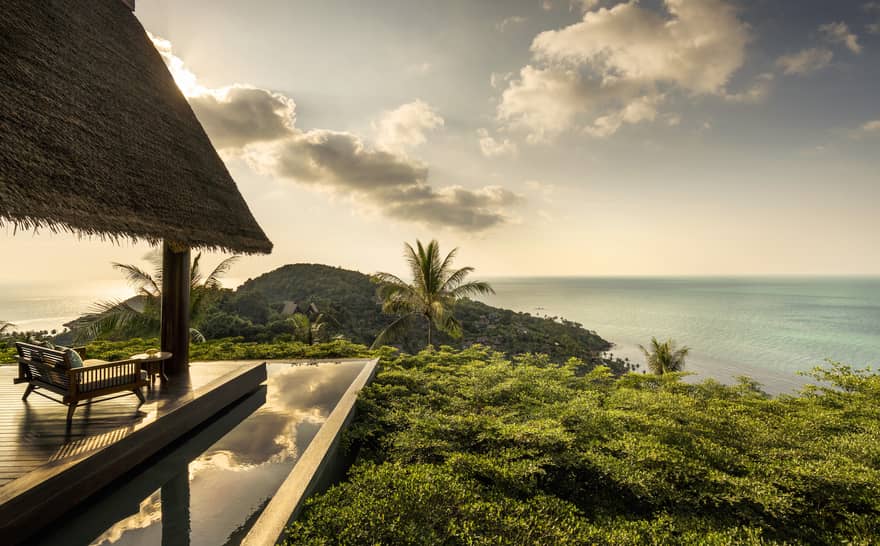 Patio lounge chair, thatched roof and deck overlooking canopy of tropical trees, ocean