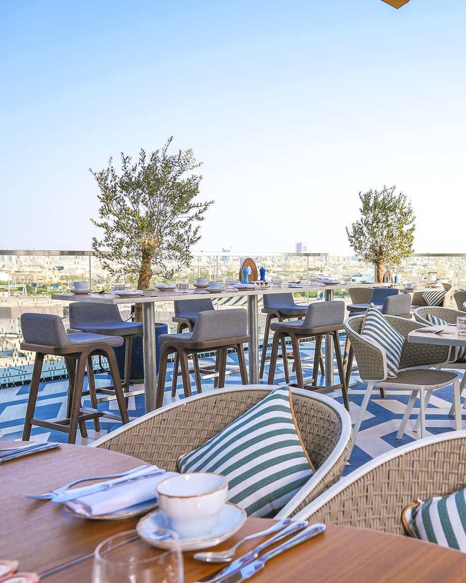 Elements' outdoor patio outfitted with rattan chairs, wood tables and a blue-and-white patterned floor, all overlooking the park with the city in the distance