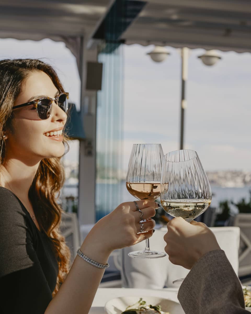 Person sitting at terrace restaurant table, toasting with a glass of wine