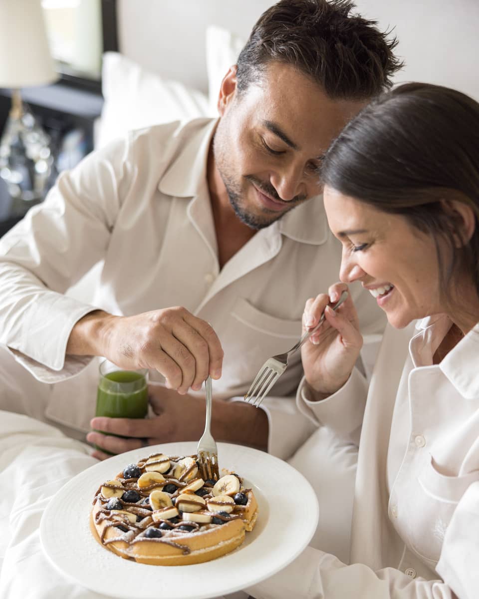 Two guests wearing pajamas and eating breakfast in bed