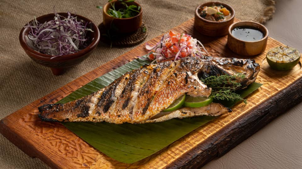 Whole Grilled Snapper served on a wooden plank along with an assortment of condiments and sauces
