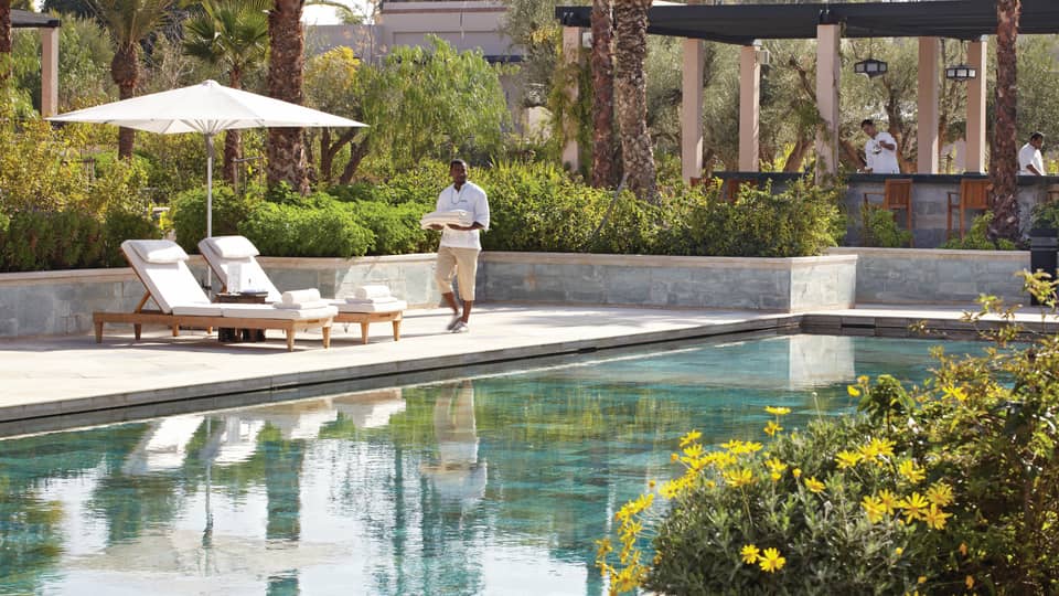 Server holding folded towels walks by lounge chairs, umbrella by adults-only outdoor swimming pool