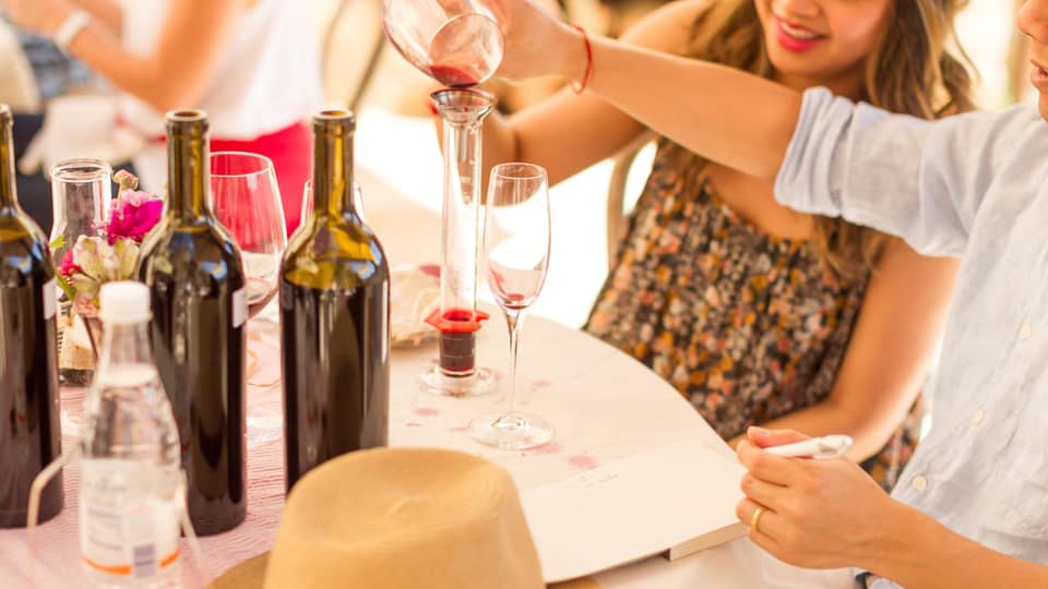 Close-up of man and woman pouring wine into glass decanter, open wine bottles on table