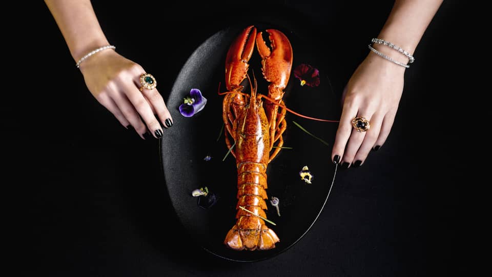 Whole lobster plated vertically on black plate with garnish