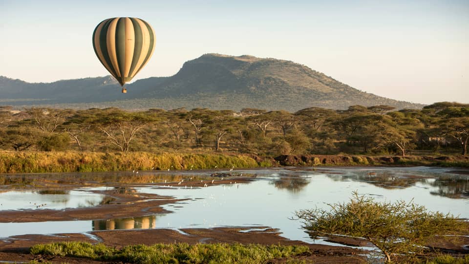 Striped hot air balloon floating over Serengeti fields, ponds