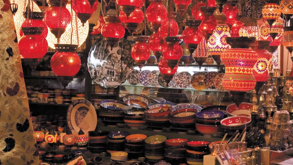 Red lanterns hang over shelves with decorative plates in Grand Bazaar