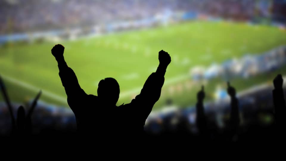 A silhouette of a person cheering at a football stadium.